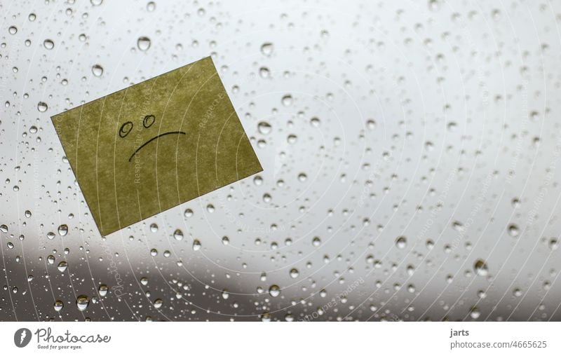 Notizzettel mit traurigem Gesicht auf einer verregneten Fensterscheibe, bei schlechtem Wetter. Regen Winter Herbst grau öde schlechtes Wetter Schlechte Laune