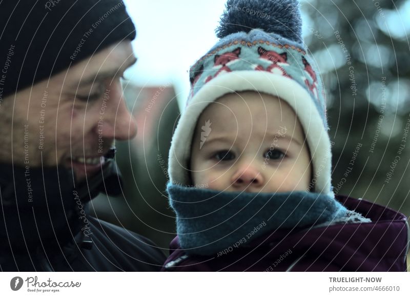 Liebevoller Vater hält seinen 1 Jahr alten, sehr aufmerksam und ernst in die Kamera schauenden Sohn draußen in der Kälte auf dem Arm Baby Kind zusammen