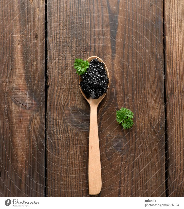 frischer körniger schwarzer Löffelstielkaviar in braunem Holzlöffel auf schwarzem Hintergrund, Ansicht von oben grün Amuse-Gueule Frühstück Kaviar Kaviare