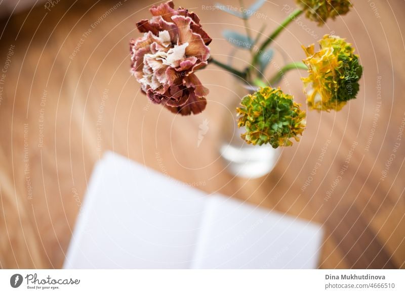 Minimalistische Blumen in einer Vase auf Holztisch und offenes Buch - Cafe Lifestyle Hintergrund mit Platz für Text und Kopie Raum. Romantische Lektüre. Floraler Hintergrund mit Tiefenschärfe.
