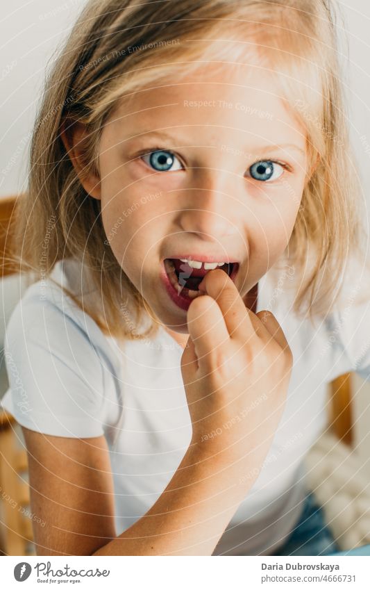 7 Jahre altes blondes Mädchen mit blauen Augen Milchzahn Lächeln mündlich Zahnmedizin Finger wenig Glück Kind Kindheit Gesicht Hintergrund jung Kaukasier