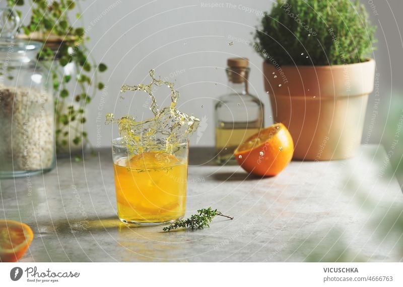Ein Spritzer Orangenlimonade mit Kräutern am Küchentisch platschen orange Limonade Küchenkräuter Tisch Glasgefäß Flasche halbiert eingetopft Wand erfrischend