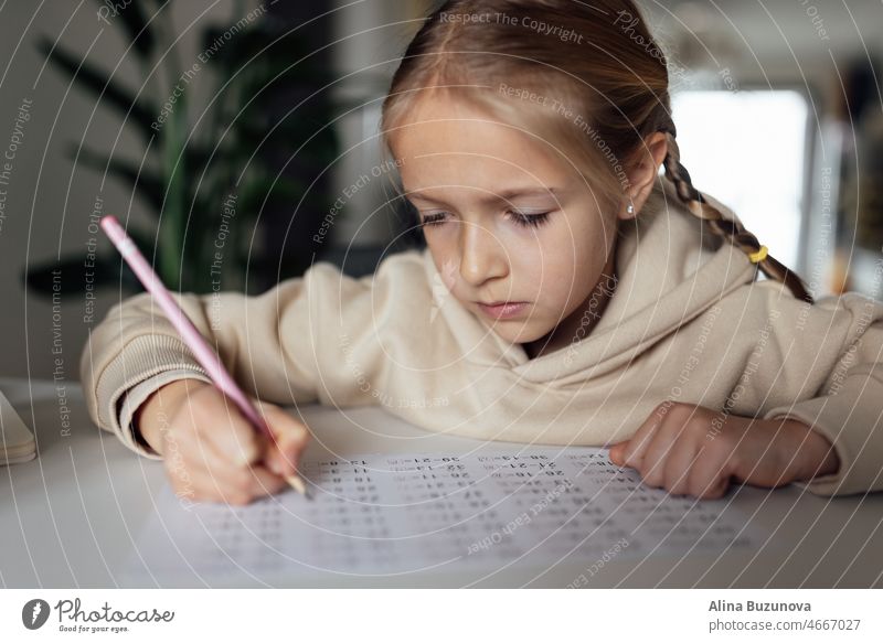 Kaukasisches Kind, das zu Hause online lernt und schreibt. Ziemlich ernsthafte Schülerin, die während der Coronavirus-Covid-19-Quarantäne und der sozialen Distanzierung Hausaufgaben in Mathematik macht