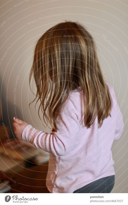 Rückansicht eines kleinen Kindes mit langen Haaren, das im Raum steht und seine Arme bewegt stehen bewegen arme turnen kinderyoga lange haare raum rücken Bücher