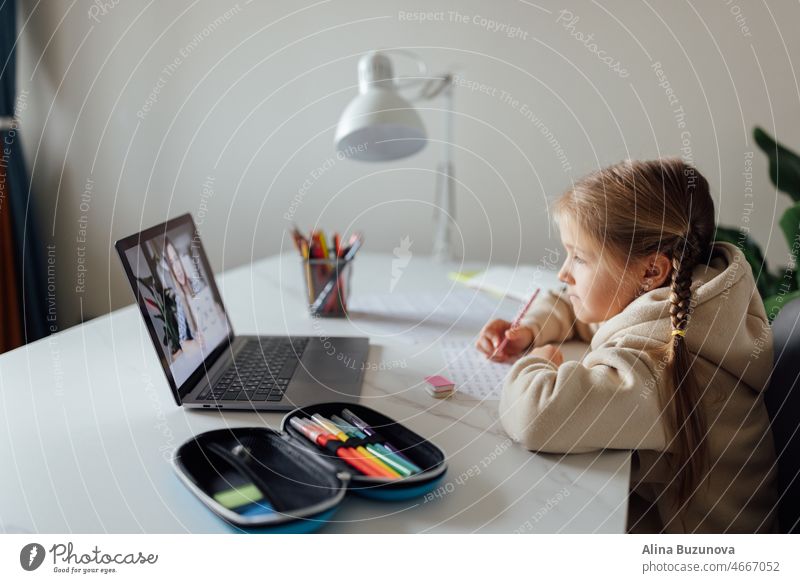 Kaukasisches Kind, das zu Hause online lernt und einen Laptop benutzt. Fernunterricht oder Fernstudium für Kinder. Hübsche, elegante Schülerin, die während der Coronavirus-Covid-19-Quarantäne und sozialer Distanzierung Hausaufgaben in Mathematik macht