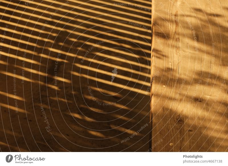 Ein Balkongitter wirft Schatten auf den Boden und die Holzbank Bank Warmes Licht Warme Farbe Sonne Menschenleer Außenaufnahme Farbfoto Tag Sonnenlicht
