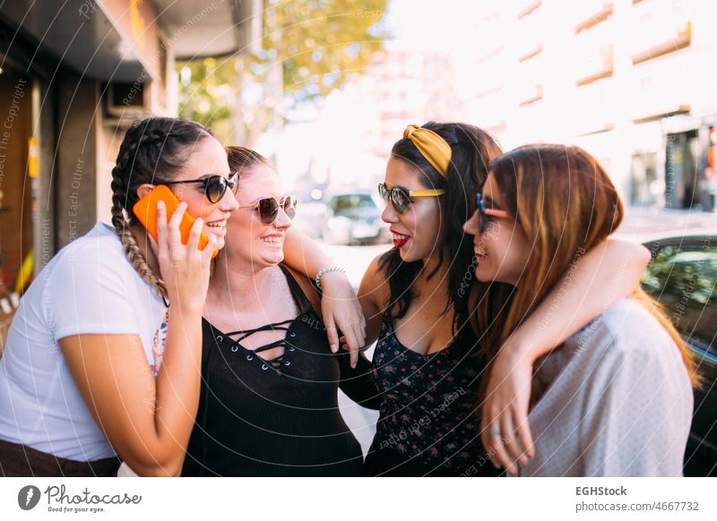 Gruppe von vier jungen Freundinnen, die sich an einem sonnigen Tag in der Stadt mit dem Mobiltelefon unterhalten, plaudernd sorgenfrei heiter Großstadt