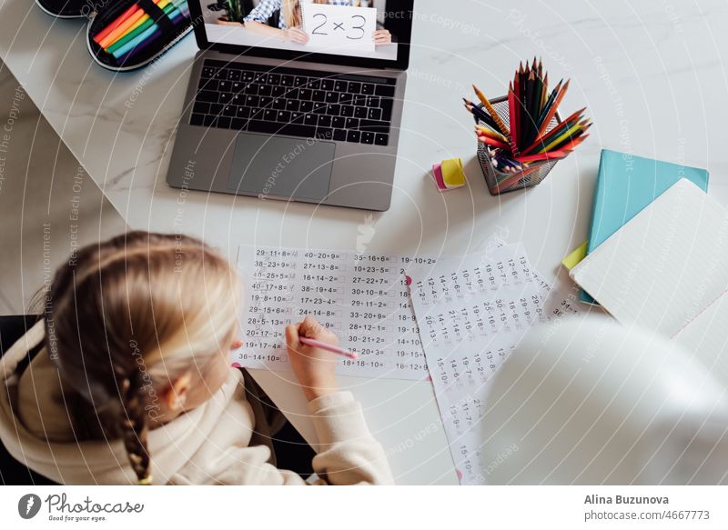 Kaukasisches Kind, das zu Hause online lernt und einen Laptop benutzt. Fernunterricht oder Fernstudium für Kinder. Hübsche, elegante Schülerin, die während der Coronavirus-Covid-19-Quarantäne und sozialer Distanzierung Hausaufgaben in Mathematik macht