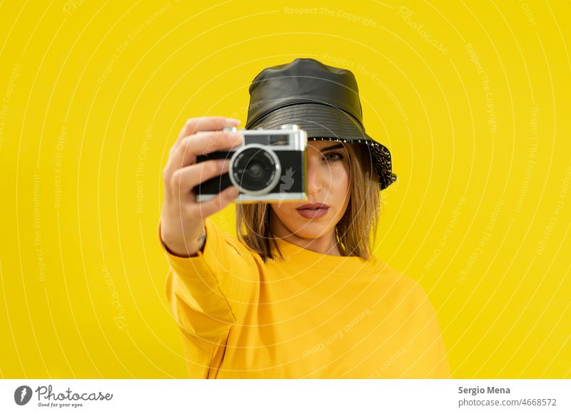 Nahaufnahme einer jungen kaukasischen Frau mit schwarzem Hut, auf gelbem Hintergrund, die eine alte Fotokamera hält Kaukasier Person schön Erwachsener Menschen