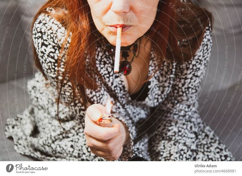 Frau mit roten langen Haaren ist dabei, sich mithilfe eines Feuerzeuges eine Zigarette anzuzünden Genusssucht ungesund Abhängigkeit Gesundheitsrisiko Tabak