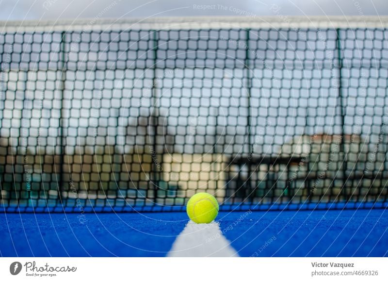 Selektiver Fokus. Ebenerdige Ansicht eines Balls auf der Linie eines blauen Paddle-Tennisplatzes mit unscharfem Netz im Hintergrund. Aktivität Leichtathletik