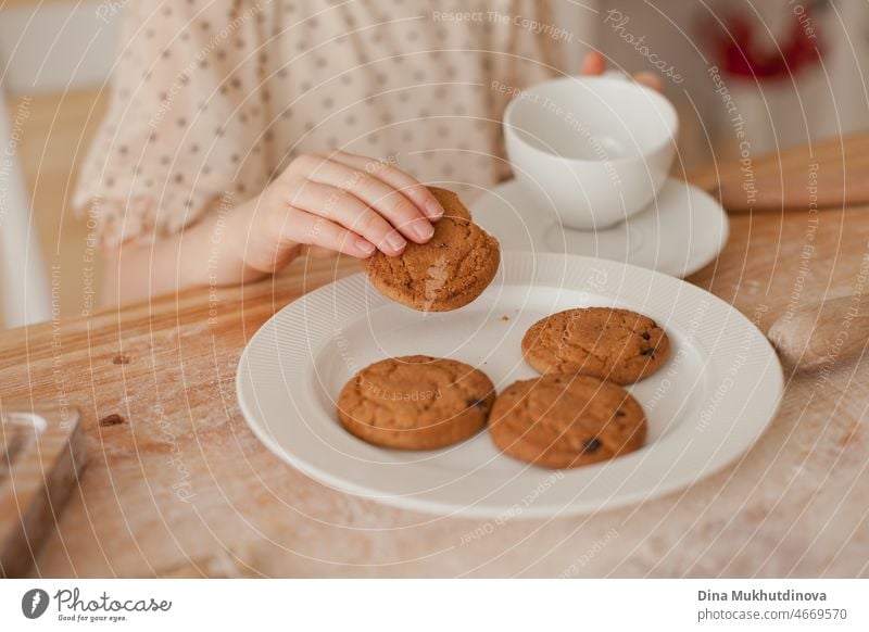 Unbekanntes junges Mädchen isst Kekse von einem weißen Teller in der Küche, während sie backt und Tee trinkt. Kind isst Nachtisch. Nahaufnahme Essen gebacken