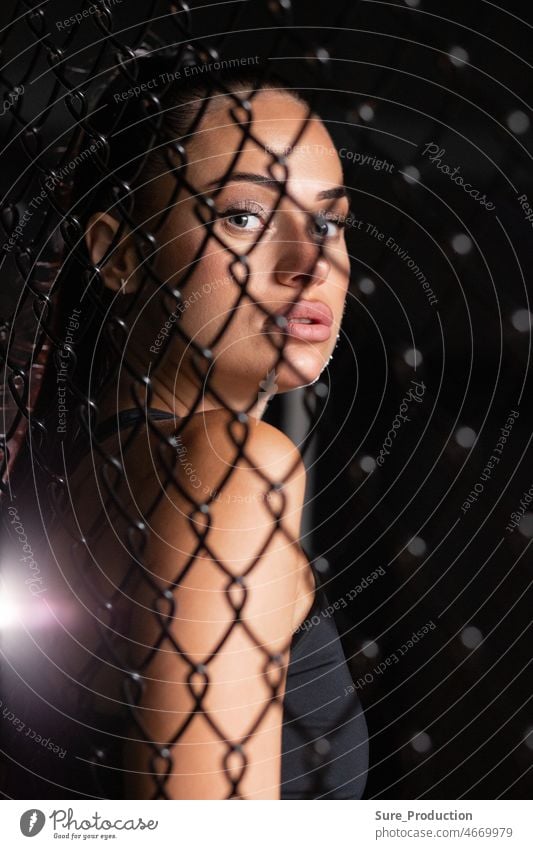 Eine Kämpferin schaut dich durch das Netz an Ein Mensch in einem dunklen Käfig hinter dem Licht bricht durch. menschlich dunkel hinten ineinander greifen Körper