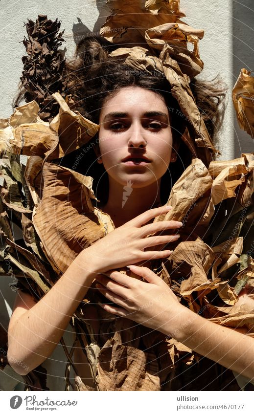 Porträt einer jungen sexy brünetten Frau, die von den Blättern eines vertrockneten Bananenbaums bedeckt ist und die Welt für den Klimawandel anklagt Mädchen