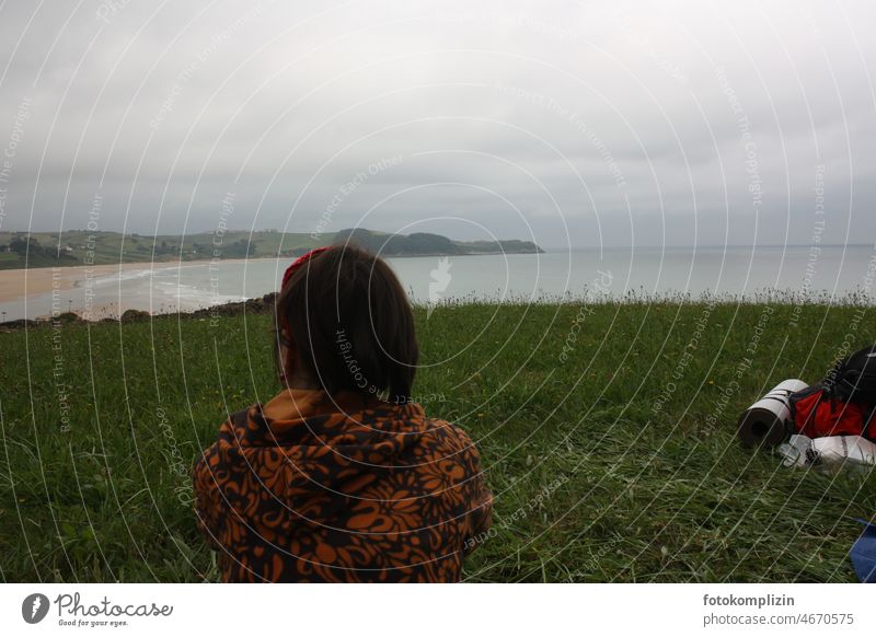 Frau blickt auf eine Meeresbucht wandern Ausblick Bucht Strand outdoor globetrotter reisen campen wildcampen Rucksack Wiese schlechtes wetter Wolken himmel