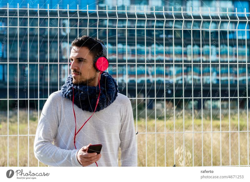 Junger Mann hört Musik über Kopfhörer und hält ein Mobiltelefon im Freien hören Smartphone Großstadt Handy Person Lifestyle urban Straße Mitteilung Telefon