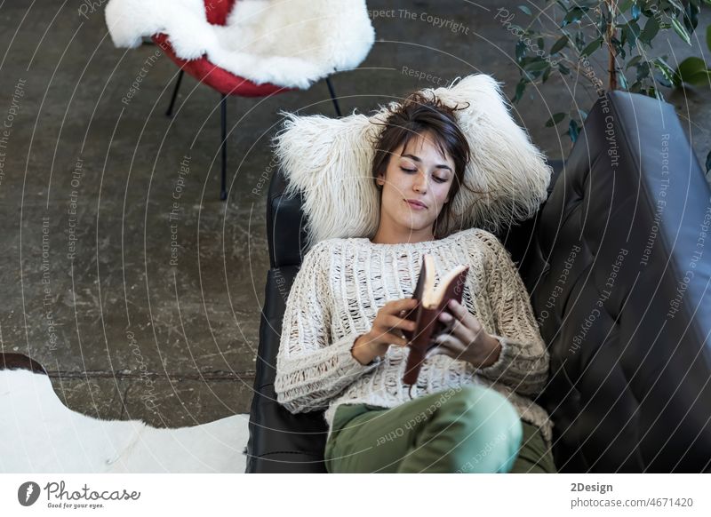 Frau liegt auf einem Sofa und liest ein Buch lesen im Innenbereich aussruhen Lügen Erholung Freizeit Liege Leder Kaukasier Lächeln Wohnzimmer Kopfkissen