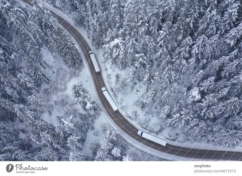 Lkw-Konvoi bei Schneefall auf einer kurvenreichen, winterlichen Bergstraße Lastwagen Straße biegend geschlängelt Landschaft Antenne Winter Laufwerk Wald Kiefern
