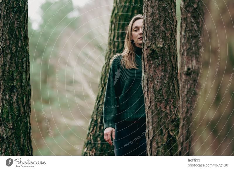 eine Frau hinter Bäumen blickt nachdenklich in die  Kamera Blick Junge Frau melancholisch Porträt besinnlich ruhig Wald Haarsträhne Natur Frauengesicht