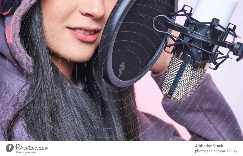 Anonyme Frau singt im Studio ins Mikrofon Sänger singen Gesang Sängerin Kopfhörer Aufzeichnen Musik Stimme Klang Kapuzenpulli Pop-Filter feminin Vorschein jung