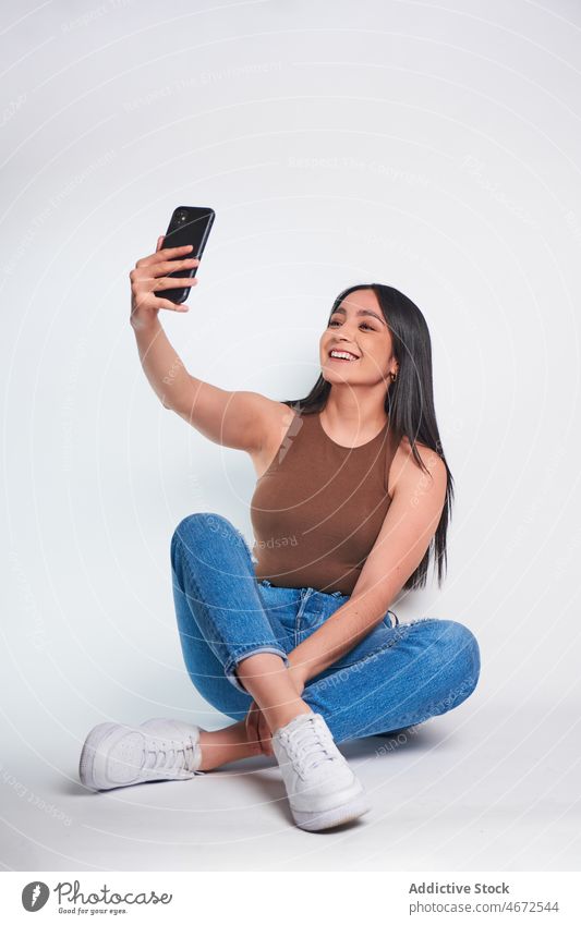 Lächelnde Frau, die im Studio ein Foto mit ihrem Smartphone macht Selfie Selbstportrait Glück soziale Netzwerke feminin fotografieren Vorschein Kleidung