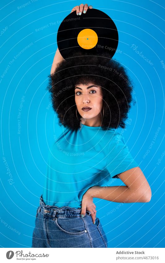 Hispanische Frau mit Schallplatte auf dem Kopf Afro-Look Vinyl Aufzeichnen retro altehrwürdig Nostalgie altmodisch meloman Stil Vorschein Frisur feminin lässig