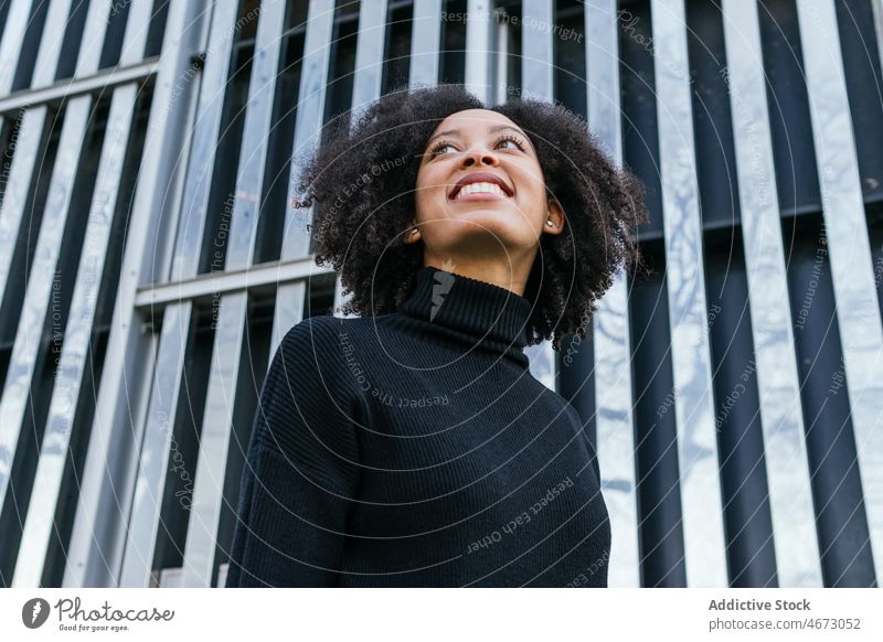 Fröhliche schwarze Frau in der Nähe der grünen Wand Straße Stil Großstadt feminin Vorschein Konstruktion Lächeln Gebäude Mode Afroamerikaner Dame Stadt Design