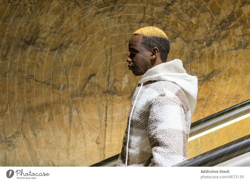 Ernster schwarzer Mann auf Rolltreppe Stil Mode U-Bahn trendy unterirdisch gefärbtes Haar Öffentlich informell Afroamerikaner modern männlich schäbig Wand