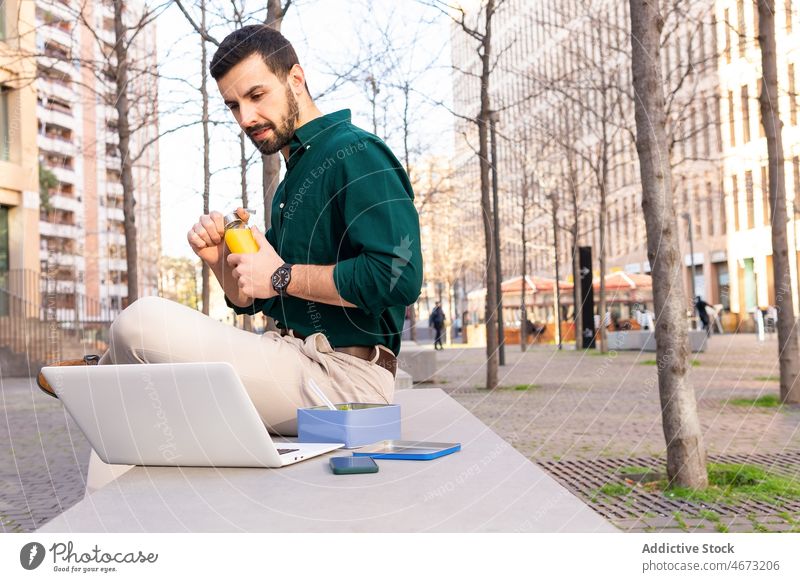 Mann mit Salat, der auf der Straße am Laptop sitzt Unternehmer Tippen Browsen online Arbeit Internet Salatbeilage Mittagessen Mahlzeit Pause Lebensmittel urban