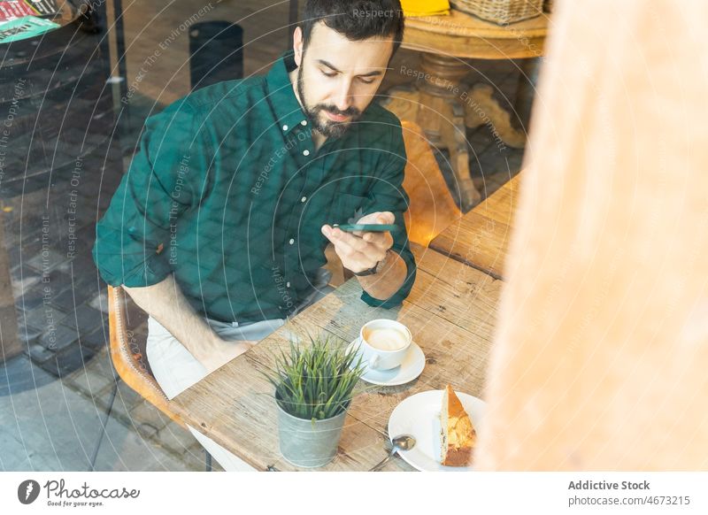 Durch das Glas eines Mannes, der in einem Café auf seinem Smartphone surft Browsen online Textnachricht Kaffee Unternehmer Pause Internet Heißgetränk Dessert