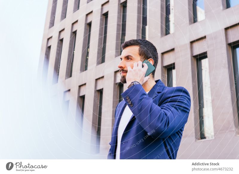 Positiver Geschäftsmann im Gespräch mit Smartphone Mann Unternehmer Straße Großstadt urban Gebäude Telefonanruf Kommunizieren diskutieren Funktelefon reden