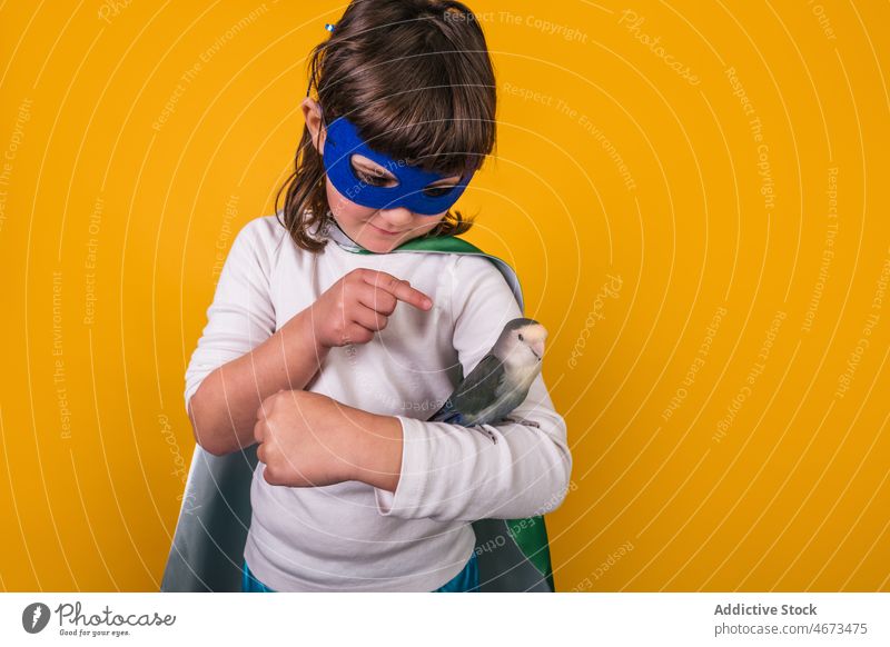 Kind im Superheldenkostüm mit Papagei Mädchen Vogel Punkt zeigen Tracht Atelier Porträt Model Mut Kraft Ehrgeiz Mundschutz Held Individualität Haustier