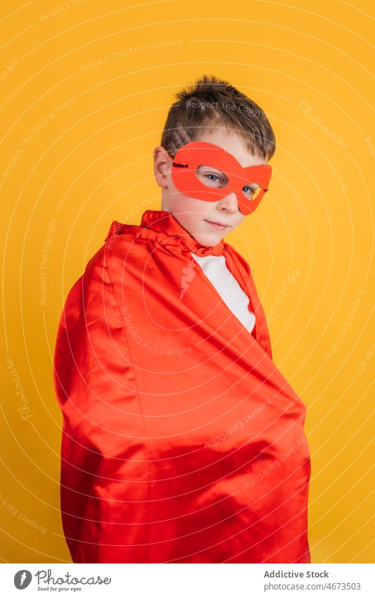 Junge mit Superheldenmaske und Umhang schaut in die Kamera im Studio Kind Tracht Mundschutz Vorschein Porträt Atelier Kraft Mut Held selbstbewusst Kap stark