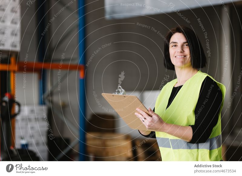 Glückliche Frau macht sich Notizen bei der Überprüfung der Vorräte Lagerhalle zur Kenntnis nehmen Lächeln schreiben prüfen Arbeit hi-vis Speicher Arbeiter