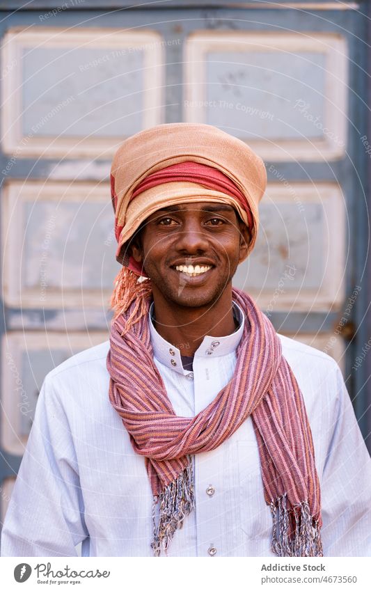 Optimistischer arabischer Mann mit Turban an einem sonnigen Tag in der Stadt Lächeln Porträt Tradition Kopfbedeckung lokal authentisch froh Zahnfarbenes Lächeln