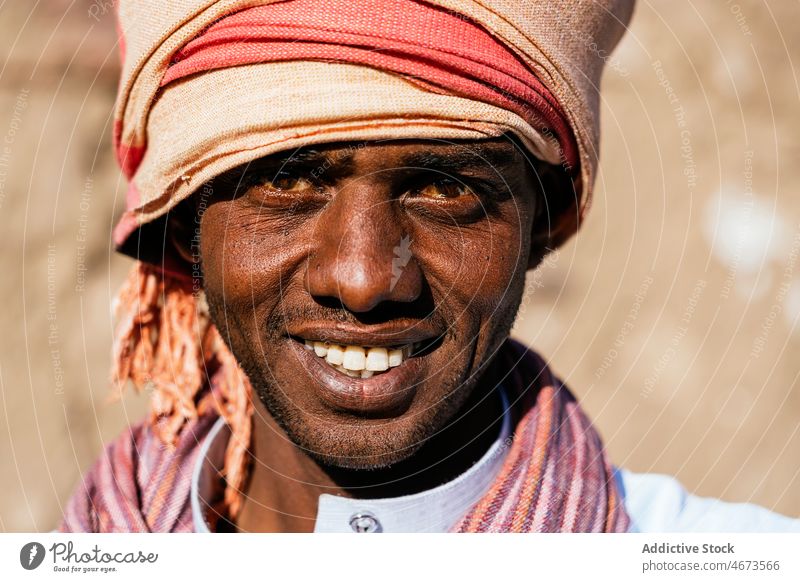 Optimistischer arabischer Mann mit Turban an einem sonnigen Tag in der Stadt Lächeln Porträt Tradition Kopfbedeckung lokal authentisch froh Zahnfarbenes Lächeln