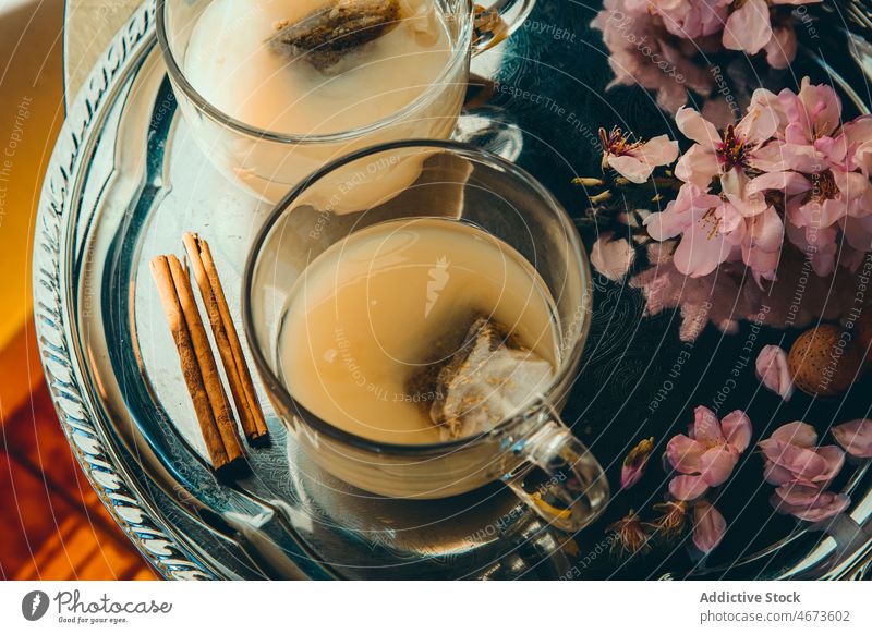 Tassen Tee mit Milch bei Blumen und Zimtstangen melken Heißgetränk Getränk Ast dienen Teetrinken geblümt Pflanze Stöcke Glas Tablett Zweig Blüte geschmackvoll