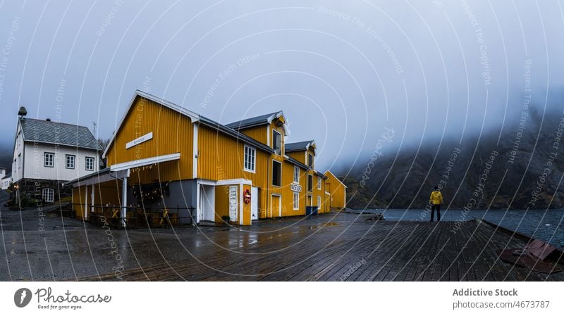 Anonymer Tourist steht auf dem Pier in der Nähe des gelben Hauses und bewundert die wilde Natur Mann bewundern Berge u. Gebirge See Reisender Fjord Nebel
