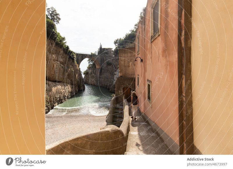 Anonyme Frau, die an einem Fluss und einem schäbigen Gebäude entlang geht Tourist Wasser Felsen Natur Reise Ausflug antik alt gealtert Italien Bogen Stein
