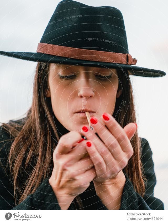 Frau mit Hut zündet Zigarette an Rauch Raucherin Beleuchtung Habitus Straße Stil Nikotin Tabak Süchtige Gelenk Dame Stadt Licht Vorschein ungesund attraktiv