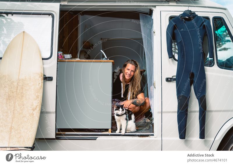 Fröhlicher Surfer mit Katze im Reisewagen Frau Anhänger Kleintransporter Lächeln Surfbrett Wohnmobil heiter Zusammensein Haustier Sommer Hobby positiv