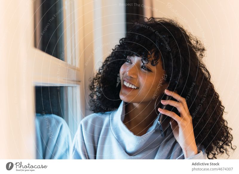 Fröhliche schwarze Frau, die zu Hause mit ihrem Smartphone spricht reden benutzend ruhen sich[Akk] entspannen Kälte online Internet Telefon Afroamerikaner