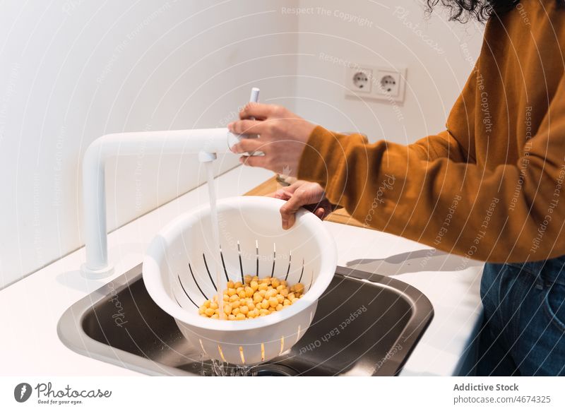 Crop-Frau wäscht Kichererbsen im Waschbecken Küche Koch Waschen gesunde Ernährung Gemüse kulinarisch vorbereiten Lebensmittel Sieb Wasser Sauberkeit Vitamin