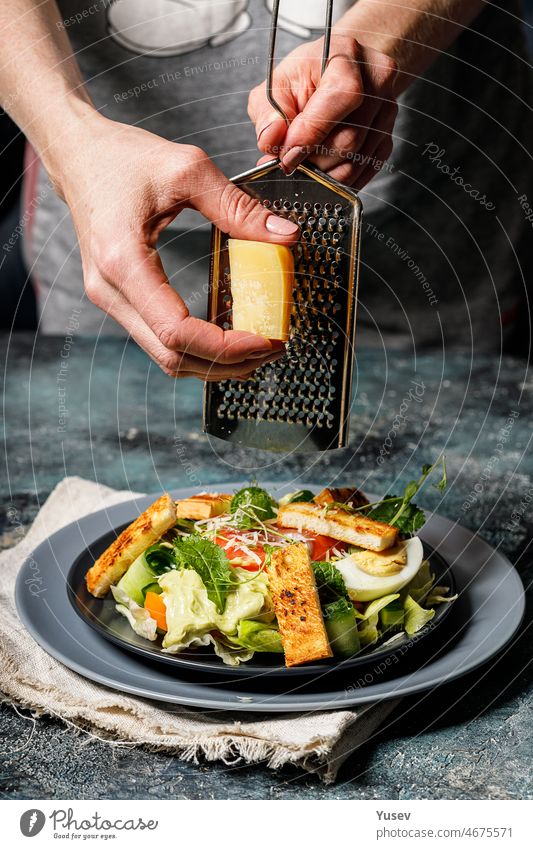 Frauenhände reiben Käse in Salat mit Lachs, Gemüse und Croutons. Mediterrane Küche. Gesunde Ernährung. Vertikale Aufnahme Hände Gitter Salatbeilage geräuchert
