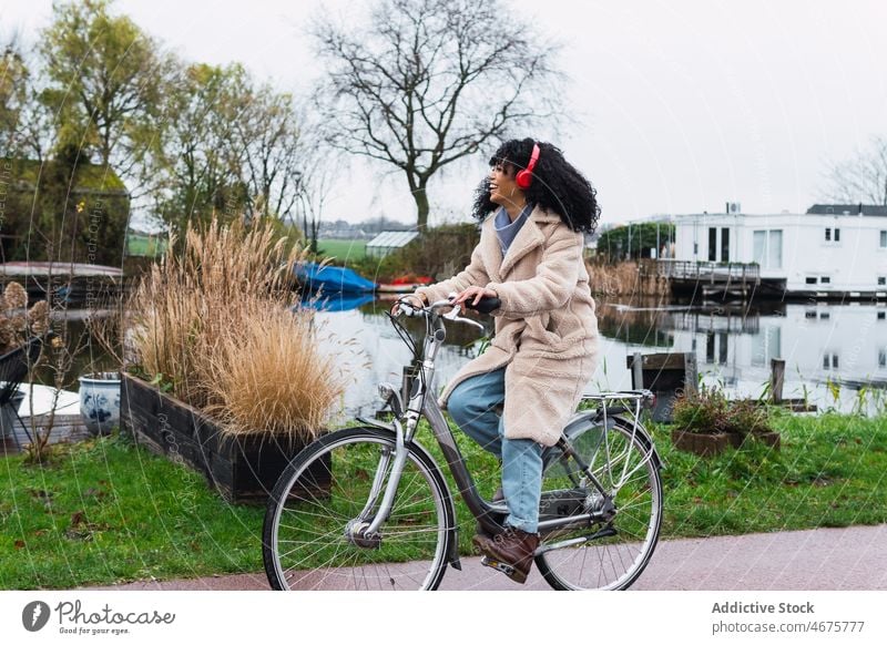 Aufgeregte schwarze Frau mit Kopfhörern beim Fahrradfahren benutzend Musik zuhören Mitfahrgelegenheit Kälte Großstadt Porträt afroamerikanische Frau