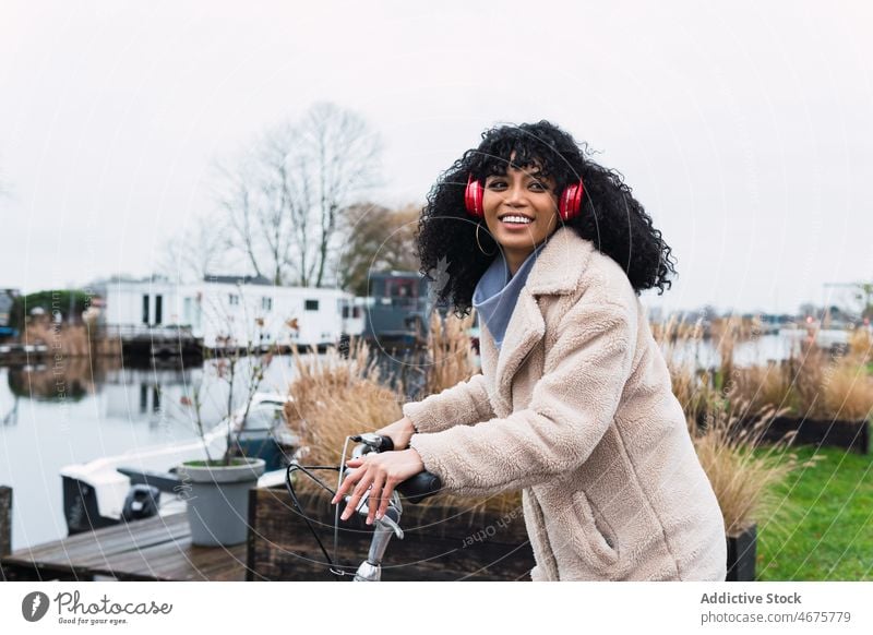 Frau mit Kopfhörern fährt Fahrrad benutzend Musik zuhören Mitfahrgelegenheit Kälte Großstadt Porträt afroamerikanische Frau schwarze Frau sich[Akk] entspannen