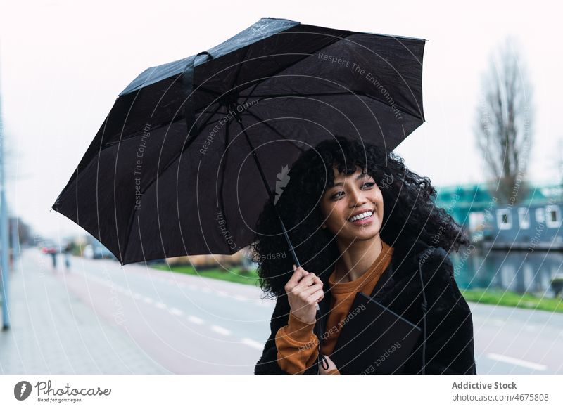 Lächelnde schwarze Frau mit Regenschirm auf der Straße Großstadt Straßenrand urban Vorschein Tablette Porträt afroamerikanische Frau lässig jung Glück positiv