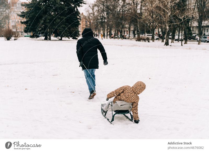Anonymer Vater, der ein fröhliches Kind auf einem Schlitten zieht Vaterschaft Kindheit Winter Schnee Vergnügen Spaß haben spielen Straße Saison Frost