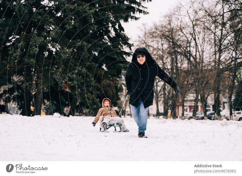 Vater, der ein fröhliches Kind auf einem Schlitten zieht Vaterschaft Kindheit Winter Schnee Vergnügen Spaß haben spielen Straße Saison Frost Oberbekleidung