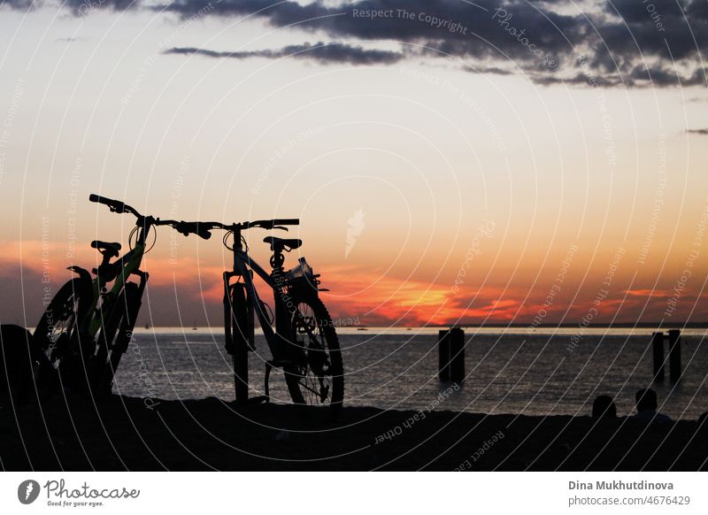 Silhouetten von Fahrrädern am Strand bei Sonnenuntergang geparkt. Fahrräder am Meer während des farbenfrohen Sonnenuntergangs. Gesunder Lebensstil und Öko-Transport.